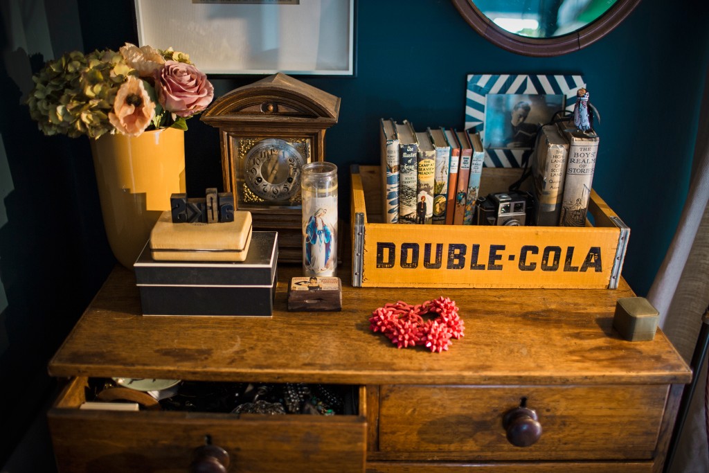 Sooz has used a colourful industrial vintage soda crate, on top of an antique oak chest of drawers to store old books, while the top shows small jewellery boxes, an old old and comtemporary photo frames, vase and flowers. 